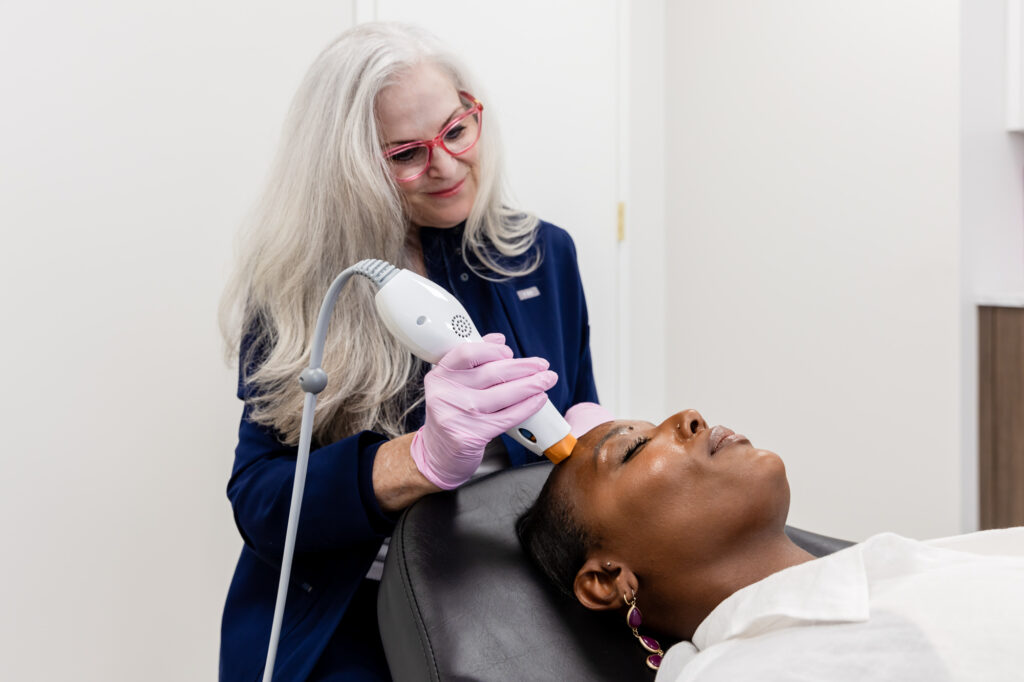 On of the top aestheticians in Philadelphia in a treatment room at About Fae Aesthetics, administering a skin tightening treatment to a young black female patient.