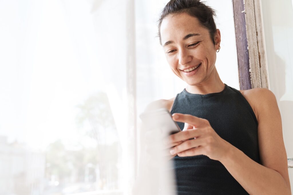 A young woman looking at her phone, leaving a positive review after her experience at About Face Aesthetics with some of the top aestheticians in Philadelphia.