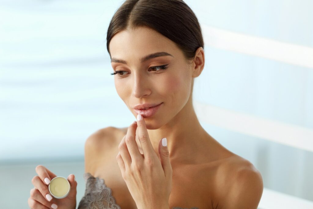 A woman applies lip balm on her lips. If she is unhappy with her lip filler, she can book an appointment for lip filler dissolving in Philadelphia at About Face Aesthetics.
