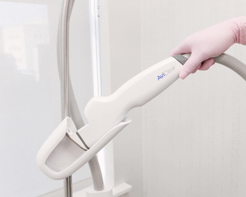 Un fournisseur d'About Face Aesthetics, portant des blouses bleu foncé et des gants roses, tient l'appareil AviClear pour le traitement des boutons près de Rittenhouse Square. Cet appareil utilise la technologie laser pour traiter la cause profonde de l’acné : le sébum.